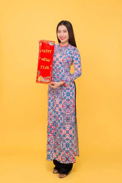 Full-length portrait of Vietnamese girl in ao-dai dress showing New Year scrolls