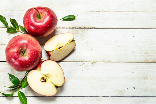 Fresh red apples with leaves. On a white wooden background.