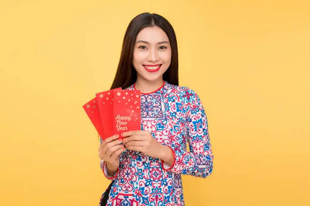 Pretty smiling Vietnamese woman with red envelopes isolated over yellow background