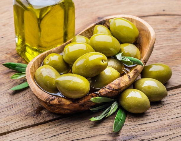 bayas de olivos y botella de aceite de oliva en la mesa de madera. - aceituna verde fotos fotografías e imágenes de stock
