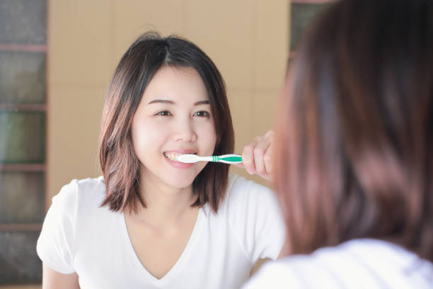 young woman brushing her teeth at mirror. after awakening - brushing teeth women toothbrush brushing imagens e fotografias de stock