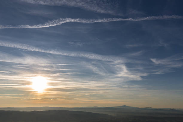 Sunset over distant mountains with blue sky full of white clouds and vapor trails