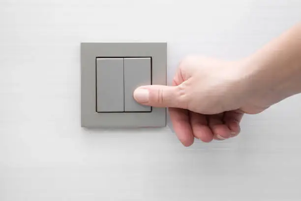 Photo of Woman's hand pressing light switch at the wall.