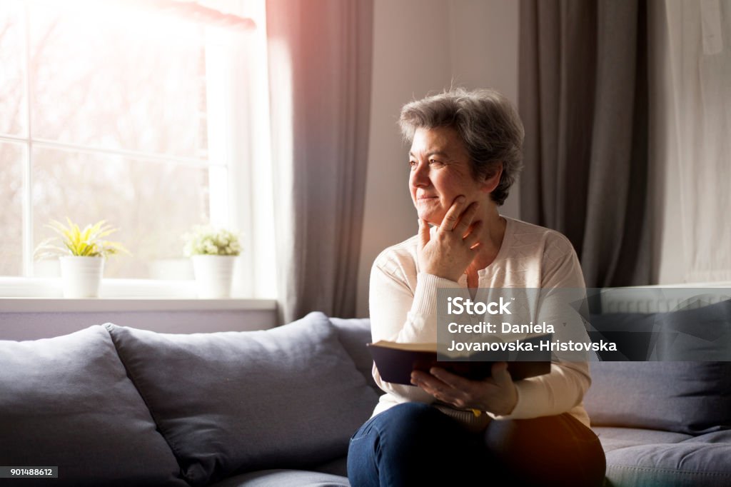 senior woman with Bible senior woman sitting on sofa reading Bible Bible Stock Photo