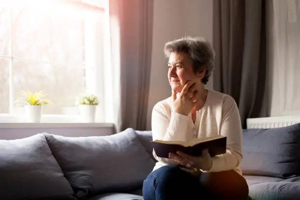 senior woman sitting on sofa reading Bible