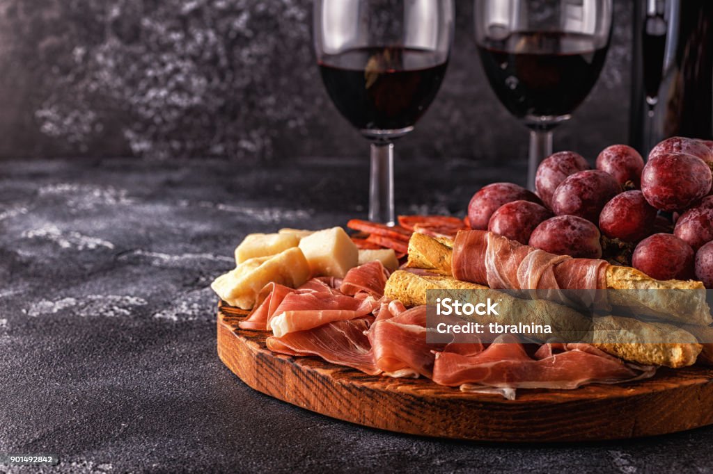 Prosciutto, sausage, wine, grape, parmesan on dark table Prosciutto, sausage, wine, grape, parmesan on dark table, selective focus. Cold Temperature Stock Photo