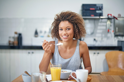 Portrait of mixed-race young woman having breakfast at kitchen.