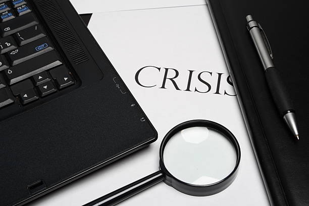 "crisis" word, laptop, magnifier, pen and notepad stock photo