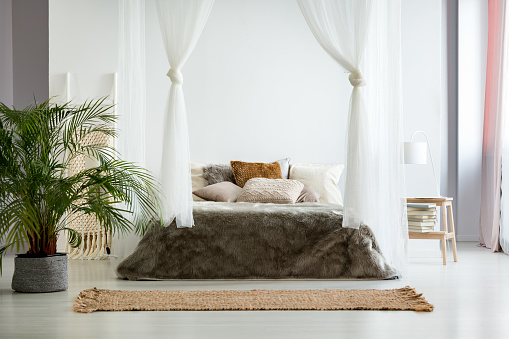 White walls and fur bedding in cozy warm bedroom with bohemian design, plants and earth color scheme