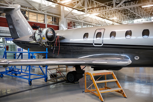 Private jet airplane in the hangar with open jet motor for regular maintenance.