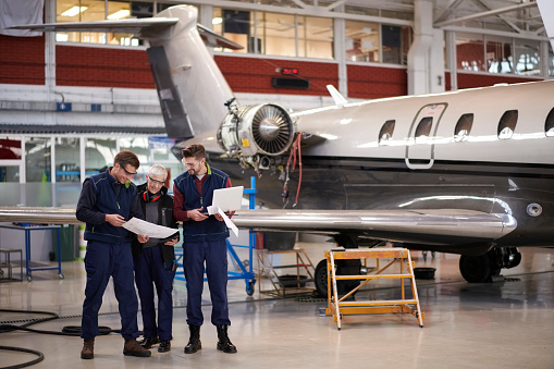 Team of three aircraft engineers in the hangar repairing and maintaining airplane jet engine.