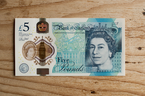 New Five pound notes on a wooden kitchen table background with Queen's head visible.