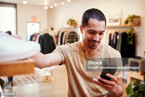 Sonriente Hombre Hispánico Con Smartphone En Una Tienda De Ropa Foto de stock y más banco de imágenes de Venta al por menor