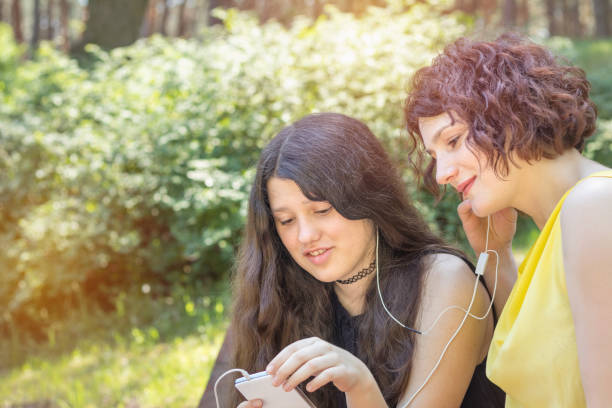 mother and teenage daughter listening to music together in the city park on a summer sunny day. walking in summer park on the summer day. copy space - parent mother music listening imagens e fotografias de stock