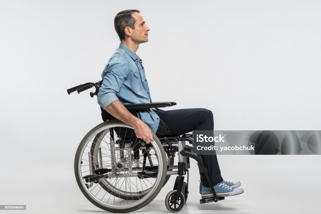 Handsome physically challenged man moving in wheelchair New start. Thoughtful concentrated handicapped man touching wheels and sitting in profile while moving ahead Wheelchair Stock Photo