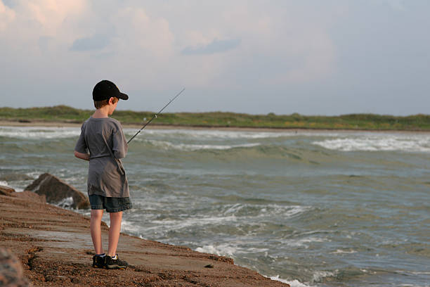 Yogyakarta, Indonesia - September 26, 2024: An Indonesian men is surf fishing at Congot Beach, Kulon Progo. Surf fishing is land-based game fishing while standing on the shoreline.