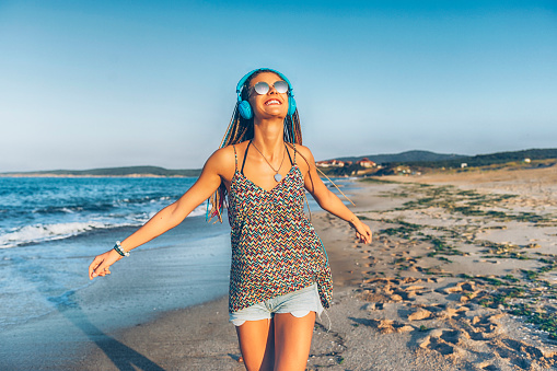 Cheerful young woman with blue headphones listening music on beach.