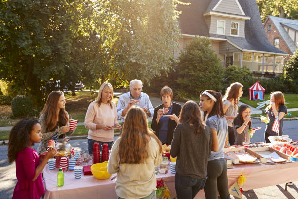 Neighbours talk and eat around a table at a block party Neighbours talk and eat around a table at a block party district stock pictures, royalty-free photos & images