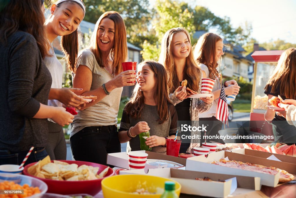 Girls stand talking at a block party food table, close up Community Stock Photo