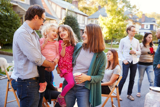 Parents holding their young kids while they eat at a block party Parents holding their young kids while they eat at a block party neighbour stock pictures, royalty-free photos & images