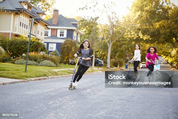 Three Preteen Girls Playing In Street On Scooters And Bike Stock Photo - Download Image Now