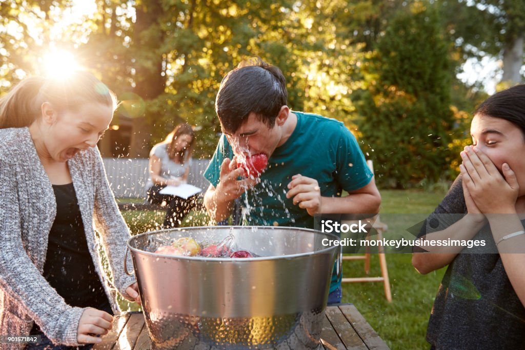 Friends watch teenage boy apple bobbing at garden party Bobbing For Apples Stock Photo
