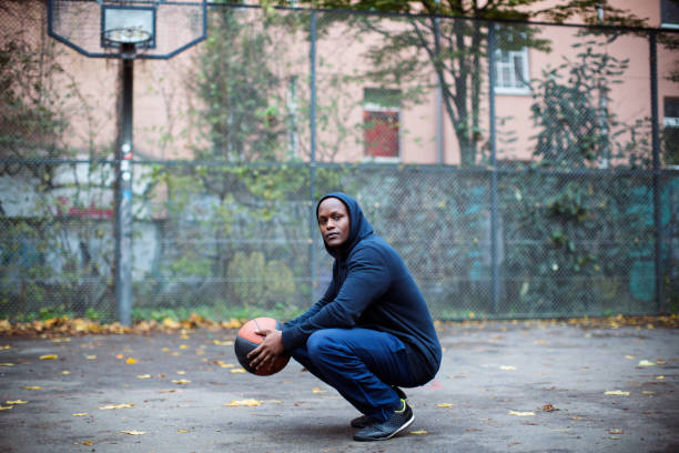 istock Man holding basketball while crouching by fence 901572168