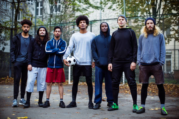 confident soccer players standing against fence - sportsman looking at camera full length sport imagens e fotografias de stock