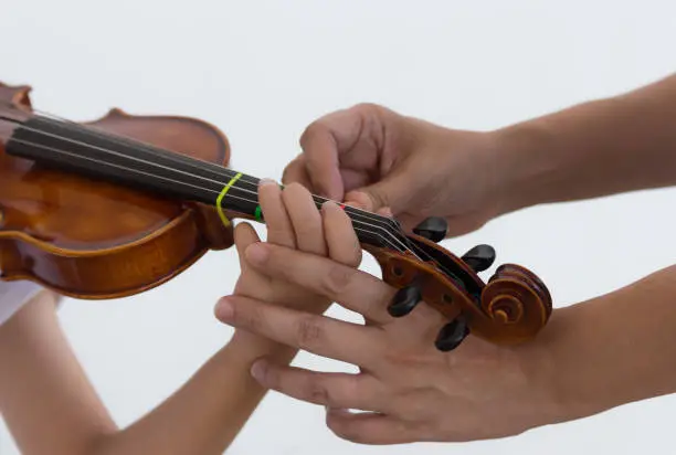 Photo of Woman's hands help kid's hand to play the violin