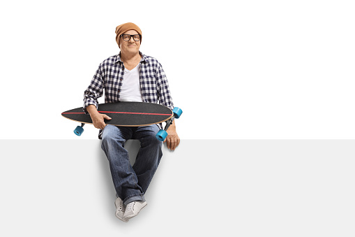 Old hipster with a longboard sitting on a panel isolated on white background