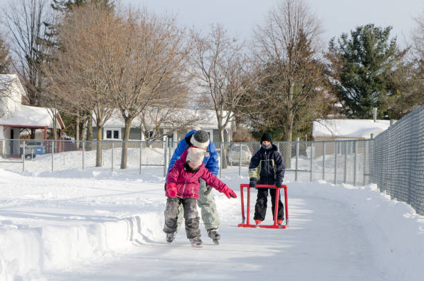 istock Mother teaching daughter how to ice skate while young boy behind uses a helping accessory 901580276