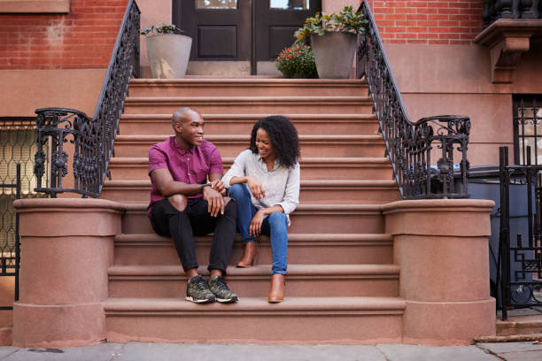 couple sit and talk on stoop of brownstone in new york city - front stoop imagens e fotografias de stock