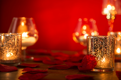 Romantic Valentine's Day scene on red background.  Scene includes: burning votive candles, rose petals.  No people.  Copy space in center.