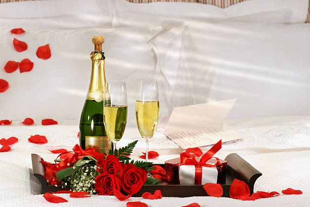 Champagne, roses, and gift waiting on romantic bed stock photo