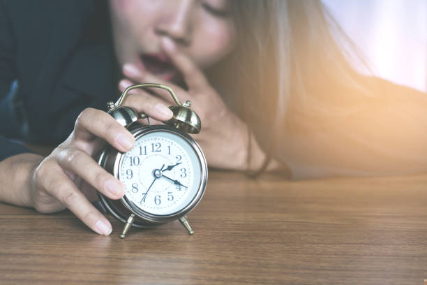 asian business woman tired from work  waking up by alarm clock and yawning still  sleepy ,office lifestyle concept background - waiting women clock boredom imagens e fotografias de stock