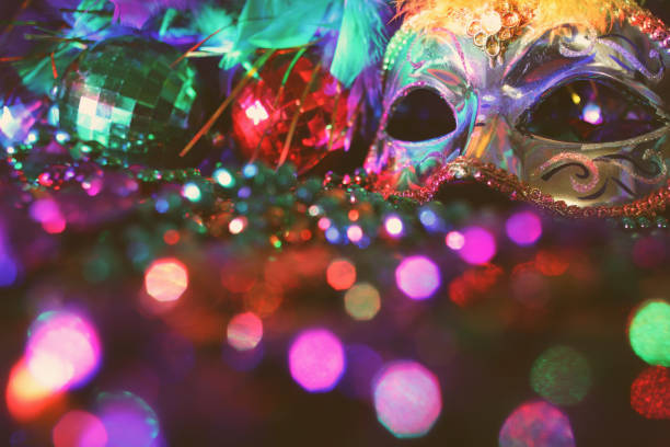 Mardi Gras, Rio carnival mask and colorful decorations. Mardi Gras or Rio Carnival mask and colorful carnival decorations. Scene includes: gold feathered mask, colored party lights, and beads. Objects lie on wooden table. No people. purple and gold masquerade masks stock pictures, royalty-free photos & images