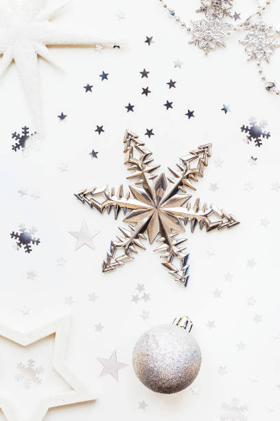 istock Christmas and New Year holiday background with decorations and light bulbs. Silver and white shining balls, white snowflakes and star confetti. Flat lay, top view. 901605068