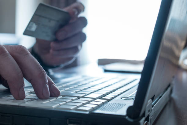 One person holds a credit card in hand and types data into a laptop
