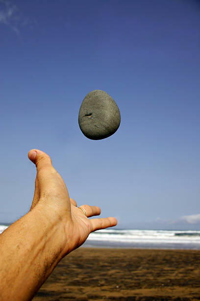a man's hand holds a large gray piece of stone on a summer street against the backdrop of green vegetation