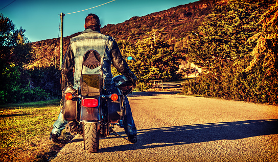 Biker on a classic motorcycle on the edge of a country road at sunset