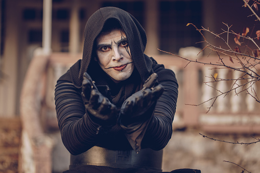 Portrait of a monk masked and dressed in black hood standing outdoors. Sect concept