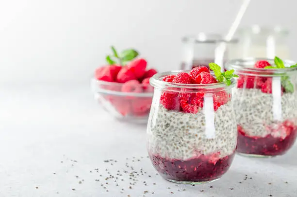 Two glass jars with chia pudding with raspberry and jam. Bowl of raspberry on the background. Horizontal image, copy space, close-up