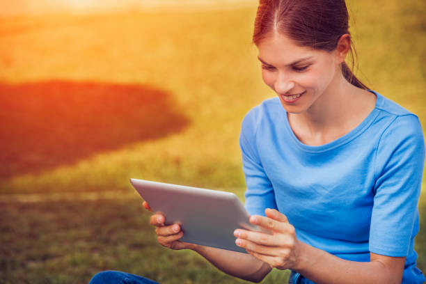istock beautiful young woman is reading from a tablet pc while seating outdoors on grass in a park 901754990