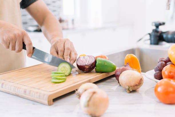 istock Hands of chef with sharp knife cutting fresh cucumbers in the kitchen at home for prepare vegetable salad. Man in kitchen concept. 901762988