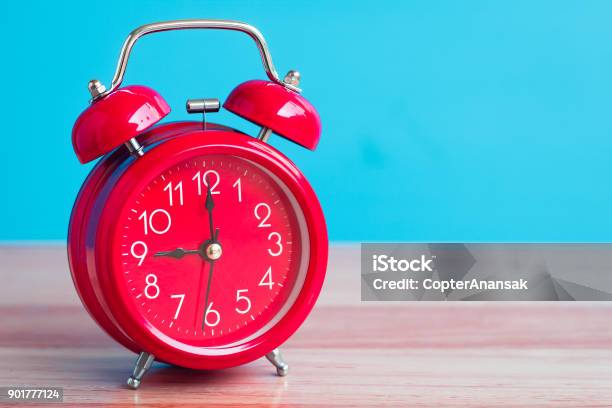 Red Clock Placed On Wooden Table On Blue Background Stock Photo - Download Image Now