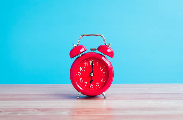 reloj rojo colocado en la mesa de madera sobre fondo azul - daylight savings fotografías e imágenes de stock
