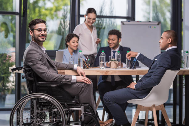 smiling disabled businessman selective focus of smiling disabled businessman looking at camera while colleagues discussing work the black womens expo stock pictures, royalty-free photos & images