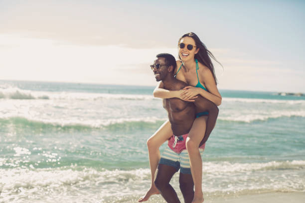 istock Cheerful man piggybacking girlfriend at beach 901805102