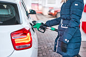 Girl in jacket fills petrol white car