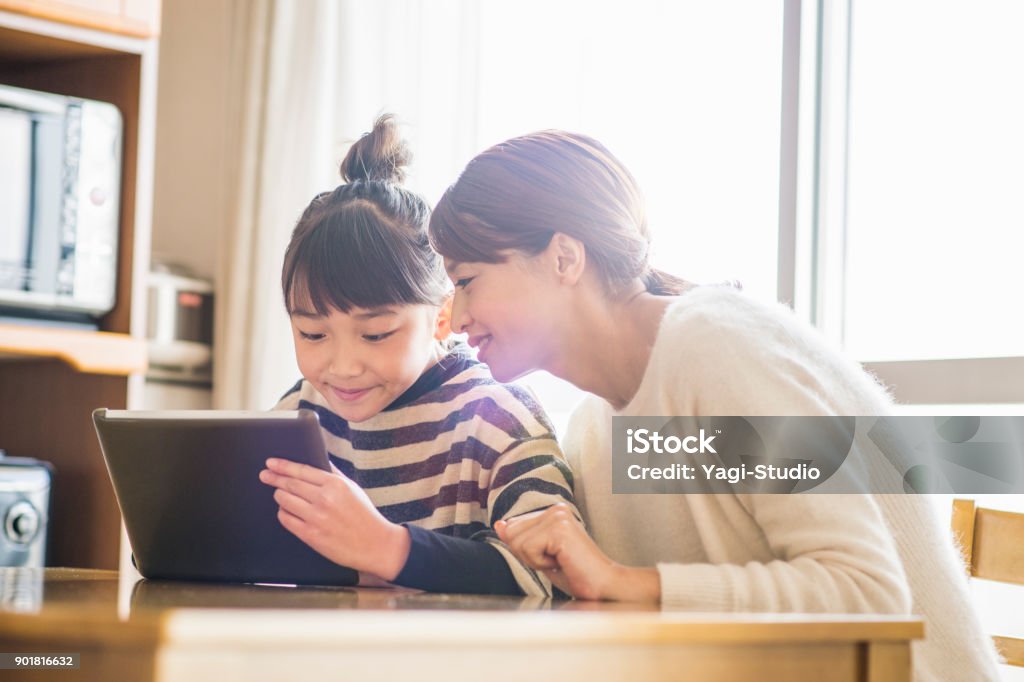 Mother and daughter playing with a digital tablet in room Girl using a digital tablet in home Child Stock Photo
